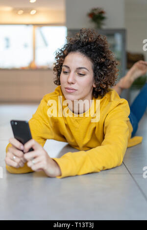 Frau auf dem Boden liegend zu Hause mit Handy Stockfoto