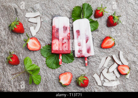 Selbstgemachte Erdbeer Kokos Eis am Stiel mit frischen Erdbeeren und Kokosnuss Scheiben auf Granit Stockfoto