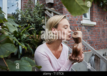 Junge Frau sitzt auf der Treppe küssen Holz- Froschkönig Stockfoto