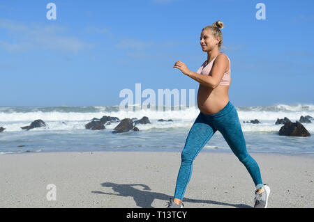 Lächelnd schwangere Frau Jogging am Strand Stockfoto