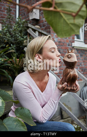 Junge Frau sitzt auf der Treppe küssen Holz- Froschkönig Stockfoto