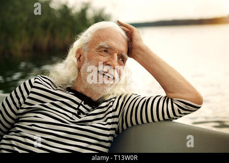 Portrait von Inhalten älterer Mann mit weissem Haar und Bart sitzt im Boot auf einem See Stockfoto