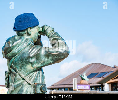 North Berwick, East Lothian, Schottland, UK, 23. März 2019. UK Wetter: sonnig Wetter im Frühling in der Stadt am Meer. Bronze Statue namens Watcher von Kenny Jäger mit eine warme Mütze Blick durch ein Fernglas Stockfoto