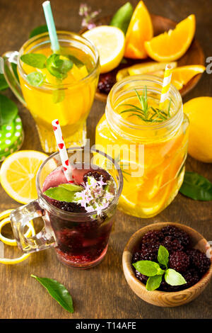 Erfrischende Sommer berry Limonade, Zitrone Tee mit Minze und Orange Limonade mit Rosmarin auf Holztisch im rustikalen Stil. Stockfoto