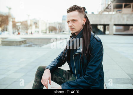 Rocker Rock Star jungen kaukasischen Mann mit Dreadlocks gehen auf die Straße der Stadt Herbst Tag. In das Leder Jacke angezogen Stockfoto