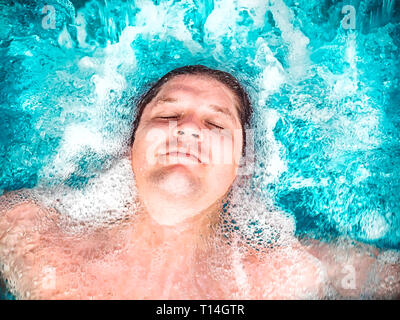 Glückliche Menschen entspannen im Whirlpool und schließen die Augen. Kaukasischen jungen ruht in einem Pool liegt im Wasser. Blick von oben. Schwimmen Kerl in einem Pool mit Stockfoto