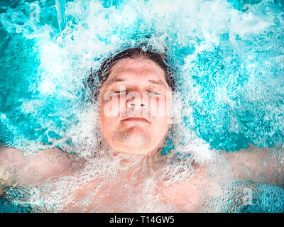 Glückliche Menschen entspannen im Whirlpool und schließen die Augen. Kaukasischen jungen ruht in einem Pool liegt im Wasser. Blick von oben. Schwimmen Kerl in einem Pool mit Stockfoto