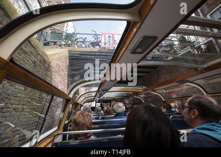 Amsterdam, Niederlande - 20 April 2017: eine tourboat nimmt Touristen um die Kanäle von Amsterdam. Das Boot geht unter einer Brücke. Klassische archit Stockfoto
