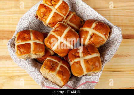 Frische Hot Cross Buns in ein Handtuch gesäumt Fach auf einer hölzernen Tischplatte Stockfoto