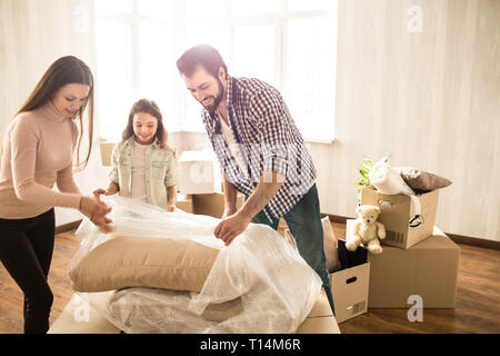 Bild von Familie auspacken Material. Sie sind von der Abdeckung, dass die Kissen und andere Sachen schützt. Sie werden dies gemeinsam tun. Auch ar Stockfoto