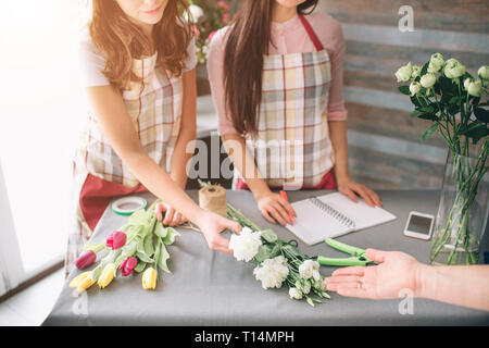 Blumen Lieferung Ansicht von oben. Floristen Ordnung schaffen, so dass Rose Bouquet im Blumengeschäft. Zwei weibliche Floristen tun Blumensträuße. Und ein Kunde Stockfoto