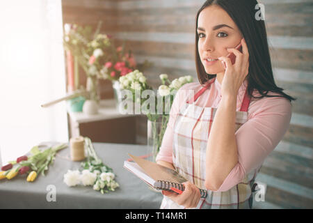Weibliche Florist bei der Arbeit: hübsche junge dunkelhaarige Frau, die Mode moderne Blumenstrauß aus verschiedenen Blumen. Frauen arbeiten mit Blumen in der Werkstatt Stockfoto