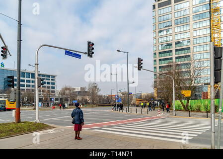 Warschau Polen. Februar 18, 2019. Ältere Frau steht vor einem fußgängerüberweg. Ampel gegen den blauen Himmel Hintergrund mit Freistellungspfad Stockfoto