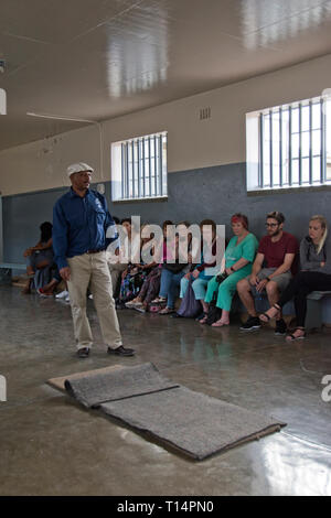Touristen hören, ein ehemaliger Häftling, der jetzt einen Reiseführer, in eine gemeinsame Zelle auf Robben Island, wo Nelson Mandela während der Apartheid inhaftiert war, Sechskantschrauben Stockfoto