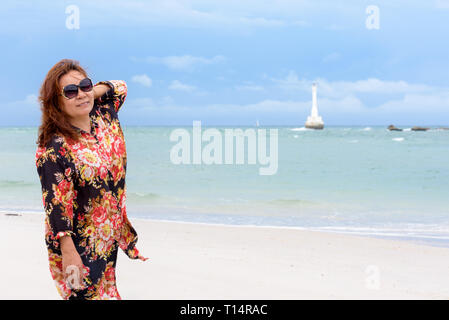 Frau mittleren Alters touristische tragen sunglasse in die Kamera schaut und lächelnd auf den Strand und das Meer im Sommer Himmel Hintergrund auf Koh Tarutao Insel, Sat Stockfoto