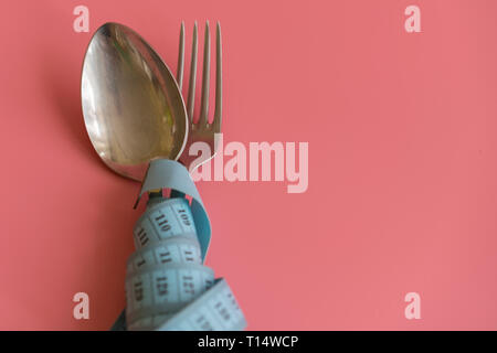 Löffel und Gabel in Maßband auf rosa Hintergrund gewickelt. Die richtige Ernährung. Medizinische verhungern. Diät für Gewicht-verlust-Konzept. Freier Platz für Text. Stockfoto