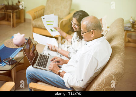 Ältere indische/asiatische Paar Buchhaltung, zu Hause finanzieren und Rechnungen mit Laptop, Rechner und Geld zu überprüfen, während auf Sofa/Couch zu Hause sitzen Stockfoto