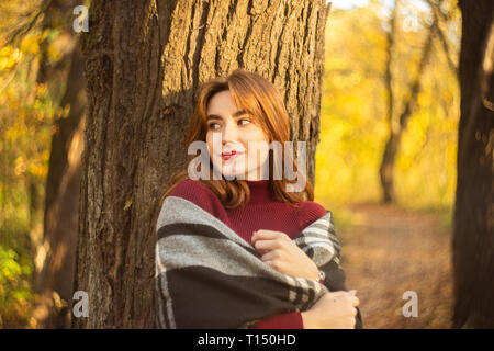 Süße Rote Haare Mädchen im Herbst Wald in der Nähe von Tree, abgesehen suchen, lächelnd Stockfoto