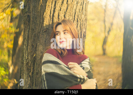 Süße Rote Haare Mädchen im Herbst Wald in der Nähe von Tree, abgesehen suchen, lächelnd Stockfoto