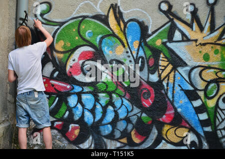 Foto in den Prozess der Ausarbeitung einer Graffiti Muster auf einem alten Betonwand. Die jungen Langhaarigen blonden Kerl zieht eine abstrakte Zeichnung in verschiedenen Farben. Stockfoto