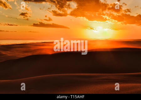 Die Sonne über Horizont hinter den langen, einsamen Dünen von Stockton Strand an der Pazifikküste von Australien - helle orange Sonnenlicht Farben Sand und s Stockfoto