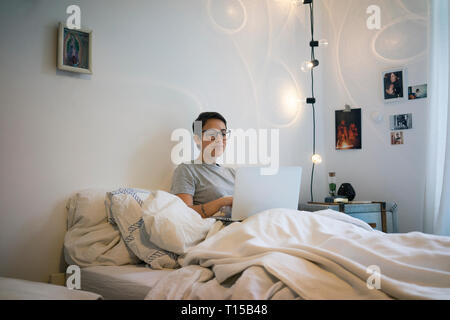 Junge Frau im Bett sitzen, mit Laptop Stockfoto