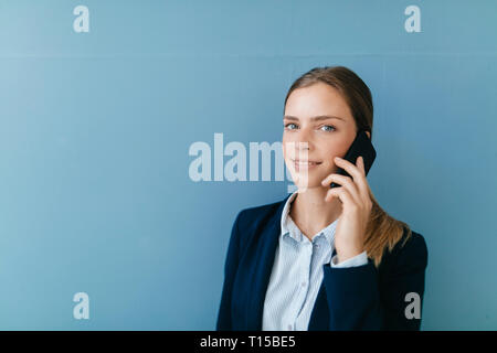 Portrait einer jungen Unternehmerin vor blauem Hintergrund, Reden auf Ihrem Smartphone Stockfoto