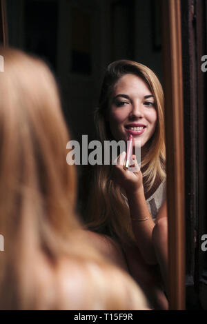 Spiegelbild der lächelnden jungen Frau Anwendung Lippenstift Stockfoto