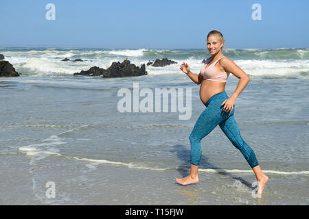 Lächelnd schwangere Frau Jogging am Strand Stockfoto