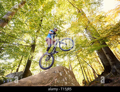 Radprofi Balancieren auf Zurück Rad Trial Bike, mann Reiter die akrobatischen Stunts am Rande des Big Boulder im Wald im Sommer sonnig Stockfoto