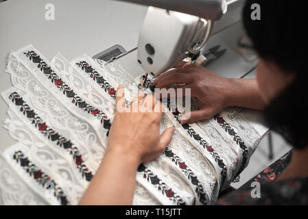 Weibliche Näherin arbeiten an modernen kompakten elektrischen Nähmaschine mit weißem Stoff details mit Blumen bunte Stickerei mit Streifen Stockfoto