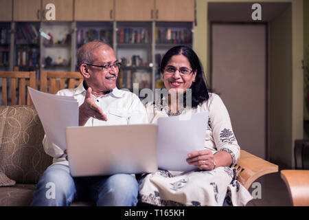 Ältere indische/asiatische Paar Buchhaltung, zu Hause finanzieren und Rechnungen mit Laptop, Rechner und Geld zu überprüfen, während auf Sofa/Couch zu Hause sitzen Stockfoto