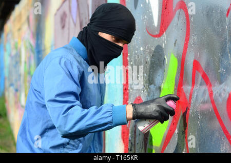 Einem jungen Hooligan mit einer versteckten Gesicht malt auf ein Metall Wand Graffiti. Illegale Vandalismus Konzept. Stockfoto