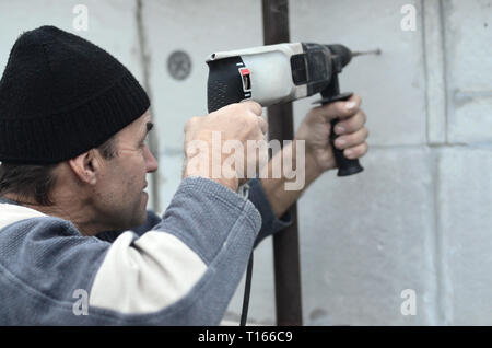 Eine ältere Arbeiter Bohrer ein Loch in einem Styropor Wand für den nachträglichen Einbau eines Kunststoff Stärkung der Dübel. Erzeugen Bohrungen in der Wand mit einem Stockfoto