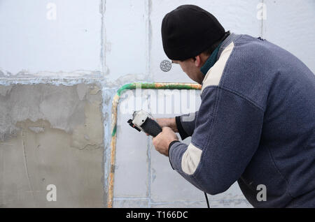 Eine ältere Arbeiter Bohrer ein Loch in einem Styropor Wand für den nachträglichen Einbau eines Kunststoff Stärkung der Dübel. Erzeugen Bohrungen in der Wand mit einem Stockfoto
