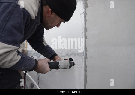 Eine ältere Arbeiter Bohrer ein Loch in einem Styropor Wand für den nachträglichen Einbau eines Kunststoff Stärkung der Dübel. Erzeugen Bohrungen in der Wand mit einem Stockfoto