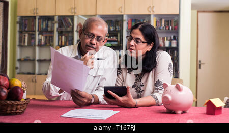 Ältere indische/asiatische Paar Buchhaltung, zu Hause finanzieren und Rechnungen mit Laptop, Rechner und Geld zu überprüfen, während auf Sofa/Couch zu Hause sitzen Stockfoto