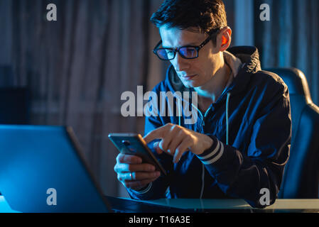 Ein junger Mann mit Brille auf einem Laptop in der Nacht arbeiten. Ein Freiberufler arbeitet an einem Projekt zu Hause. Stockfoto