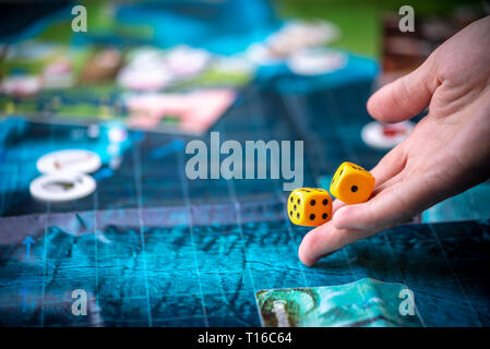 Die Hand wirft zwei gelbe Würfel auf das blaue Feld der Fantasy Spiel. Gaming Momente in der Dynamik. Glück und Aufregung. Konzept Gesellschaftsspiele Strategie Stockfoto