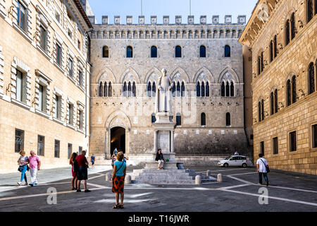 Siena, Italien - 27. August 2018: historischen, mittelalterlichen Altstadt Dorf in der Toskana mit Statue im Palazzo Salimbeni Bandini und Menschen zu Fuß im Quadrat Stockfoto