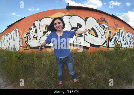 Porträt eines emotionalen junge Mädchen mit schwarzen Haaren und Piercings. Ein Foto eines Mädchens mit Aerosol Sprühdosen in der Hand auf einem Graffiti Wal Stockfoto