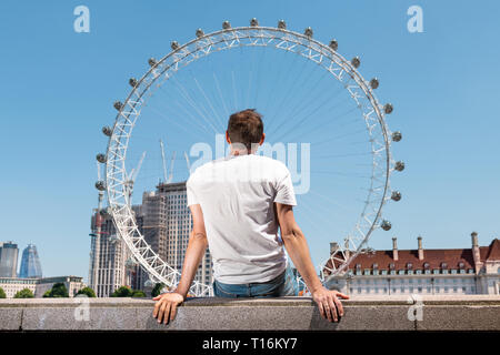 Zurück junger Mann sitzt auf Geländer im Stadtbild Skyline der Stadt mit der Themse und London Eye in Vereinigtes Königreich suchen während der sonnigen Sommer Stockfoto