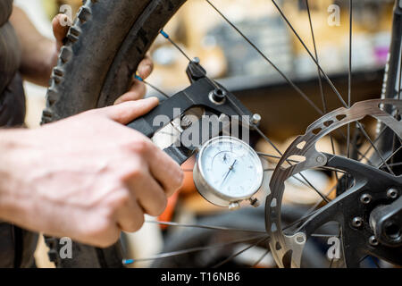 Mann Ausrichten eines Fahrrades, Kontrolle der Nadeln Stretch mit speziellen Werkzeug am Arbeitsplatz, Nahaufnahme Stockfoto