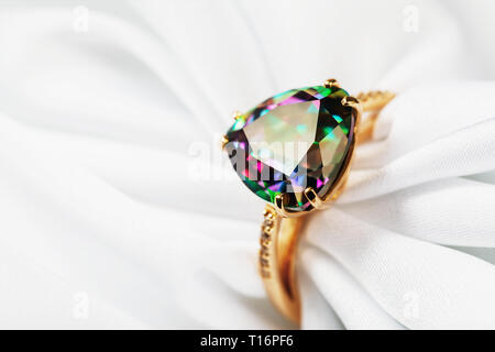 Schönen Gold Ring mit einem großen Edelstein, irisierend in verschiedenen Farben auf einem weißen Seide, closeup geschmückt Stockfoto