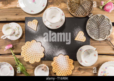 Leckere Waffeln, traditionellen alten Waffeleisen auf rustikale Holzplanken mit Schiefer und englische Porzellan angeordnet. Von oben, flach Schuß. Stockfoto