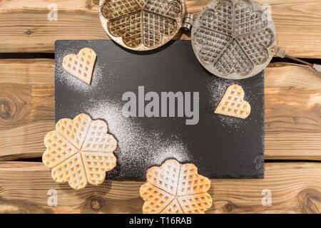 Leckere Waffeln, traditionellen alten Waffeleisen auf rustikale Holzplanken mit Schiefer und englische Porzellan angeordnet. Von oben, flach Schuß. Stockfoto