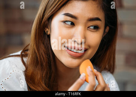 Closeup jungen asiatischen positive Frau Anwendung Pulver auf glänzenden Gesicht auf unscharfen Hintergrund Stockfoto