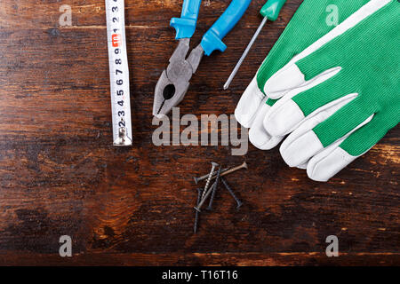 Arbeitshandschuhe und Tischler Werkzeuge auf einem braunen Holztisch liegen. Blick von oben. Platz für Text Stockfoto