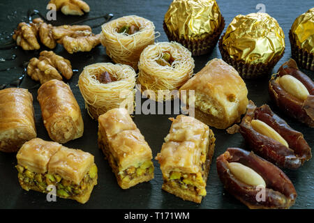 Andere Art von arabischen Süßigkeiten Hintergrund baklava borma Nest ush-el-bul-bul asabi Termine und Schokolade auf schwarzen Stein Hintergrund Stockfoto