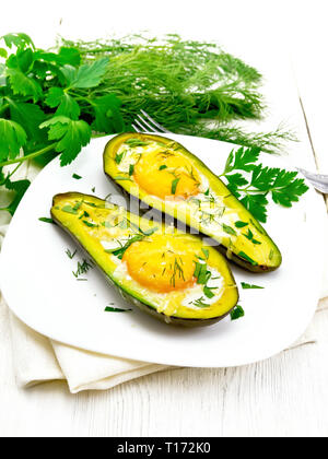 Rührei mit würzigen Grünen in zwei Hälften von Avocado in eine Platte auf Serviette, Gabel, Petersilie auf dem Hintergrund der hellen Holzmöbeln board Stockfoto